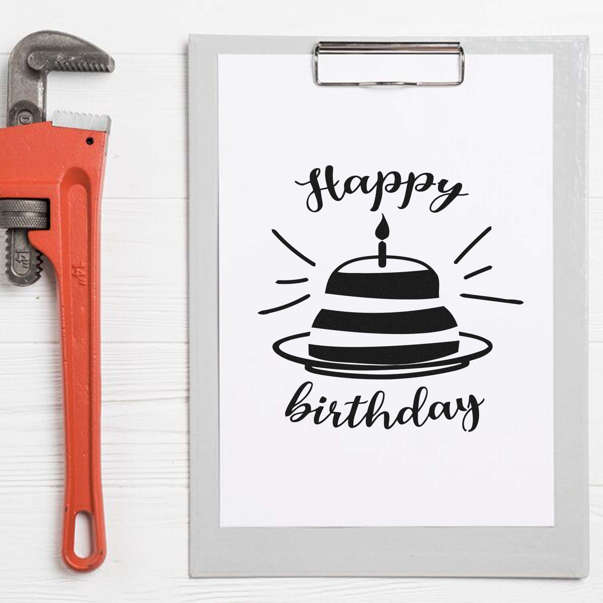 Custom stamp and seal set with black Happy Birthday cake design on clipboard, beside orange pipe wrench.