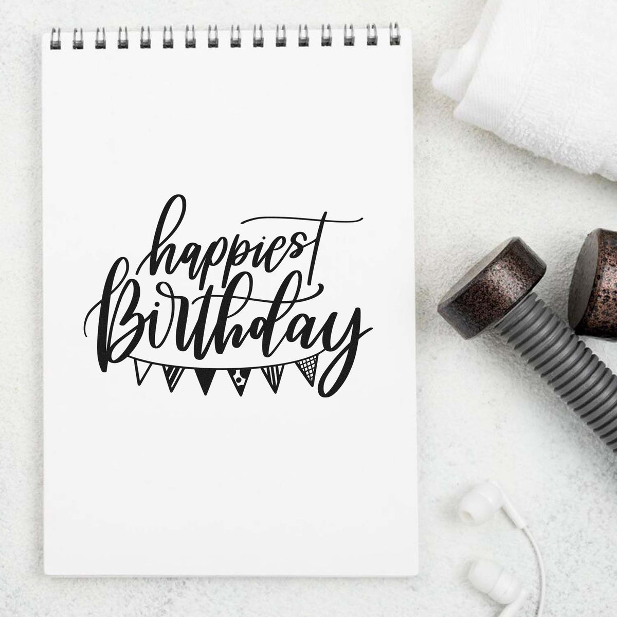 Black "happiest birthday" stamp on white notepad with spiral binding, beside brown stamp seal tools on a white background.