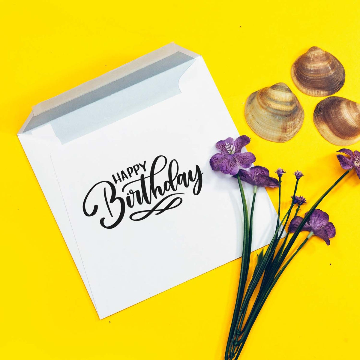 Birthday stamp seal on a white envelope, with purple flowers and seashells on a bright yellow background.