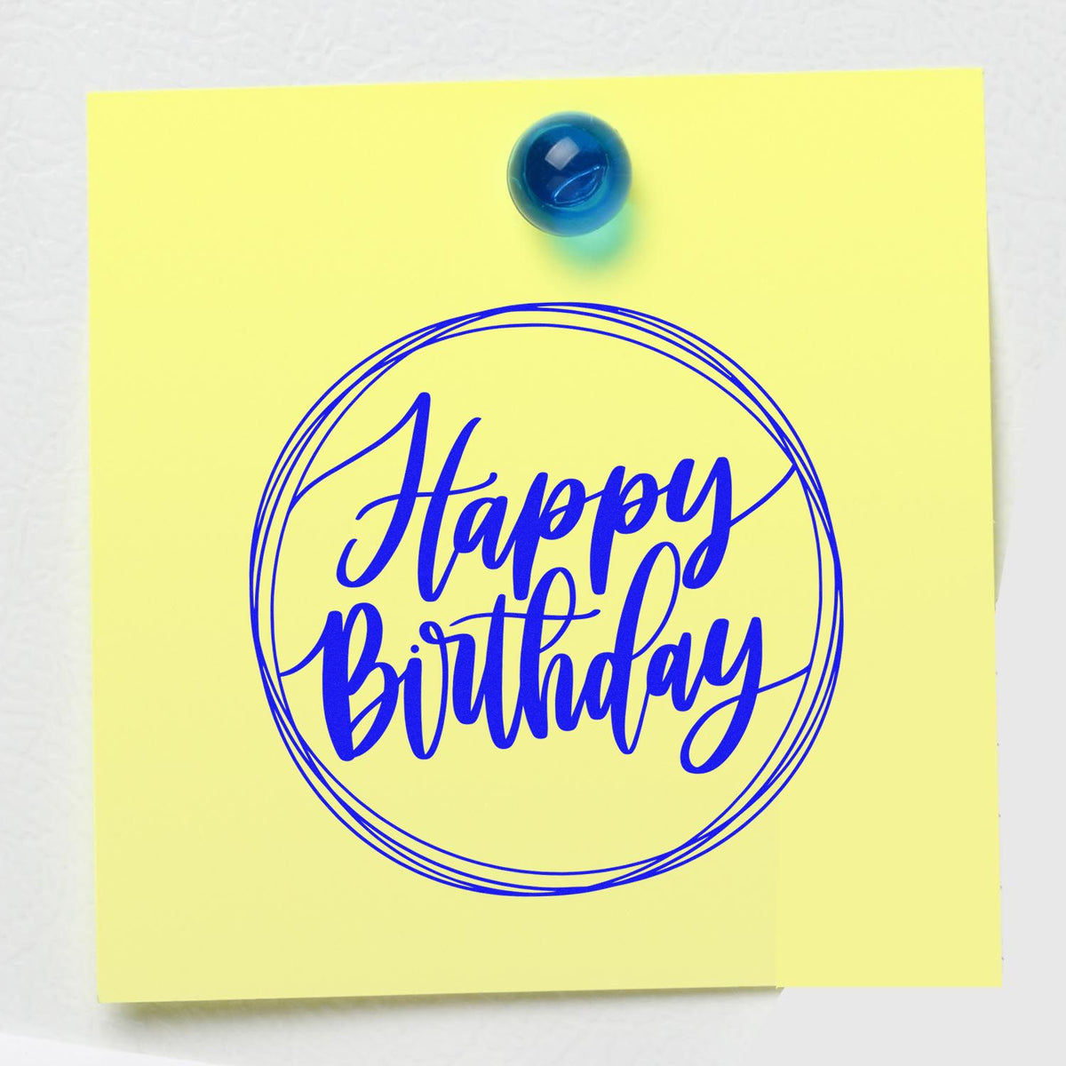 Yellow note with blue Happy Birthday round stamp seal and matching blue push pin.