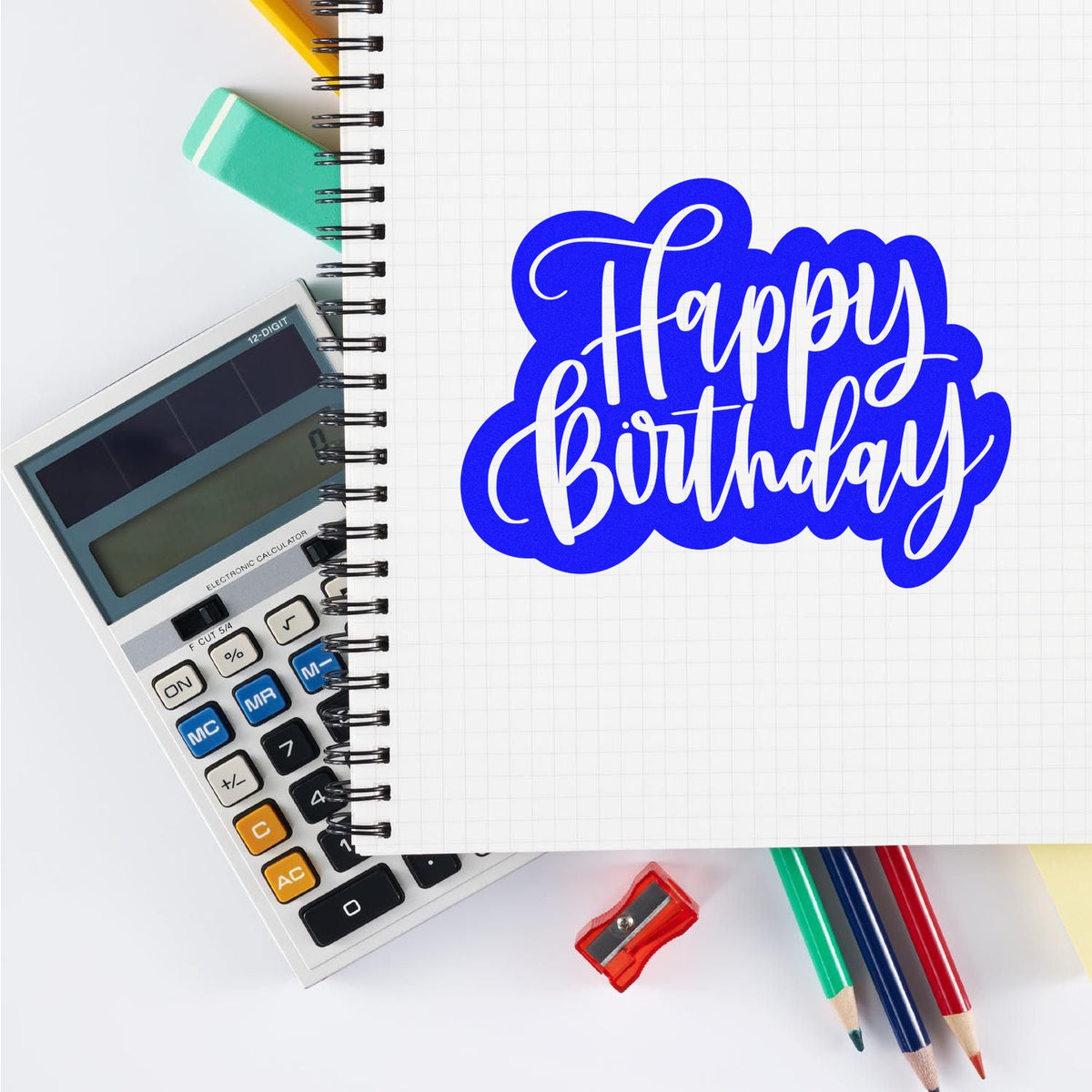 Blue Happy Birthday stamp seal on graph notebook with calculator, pencils, and sharpener.