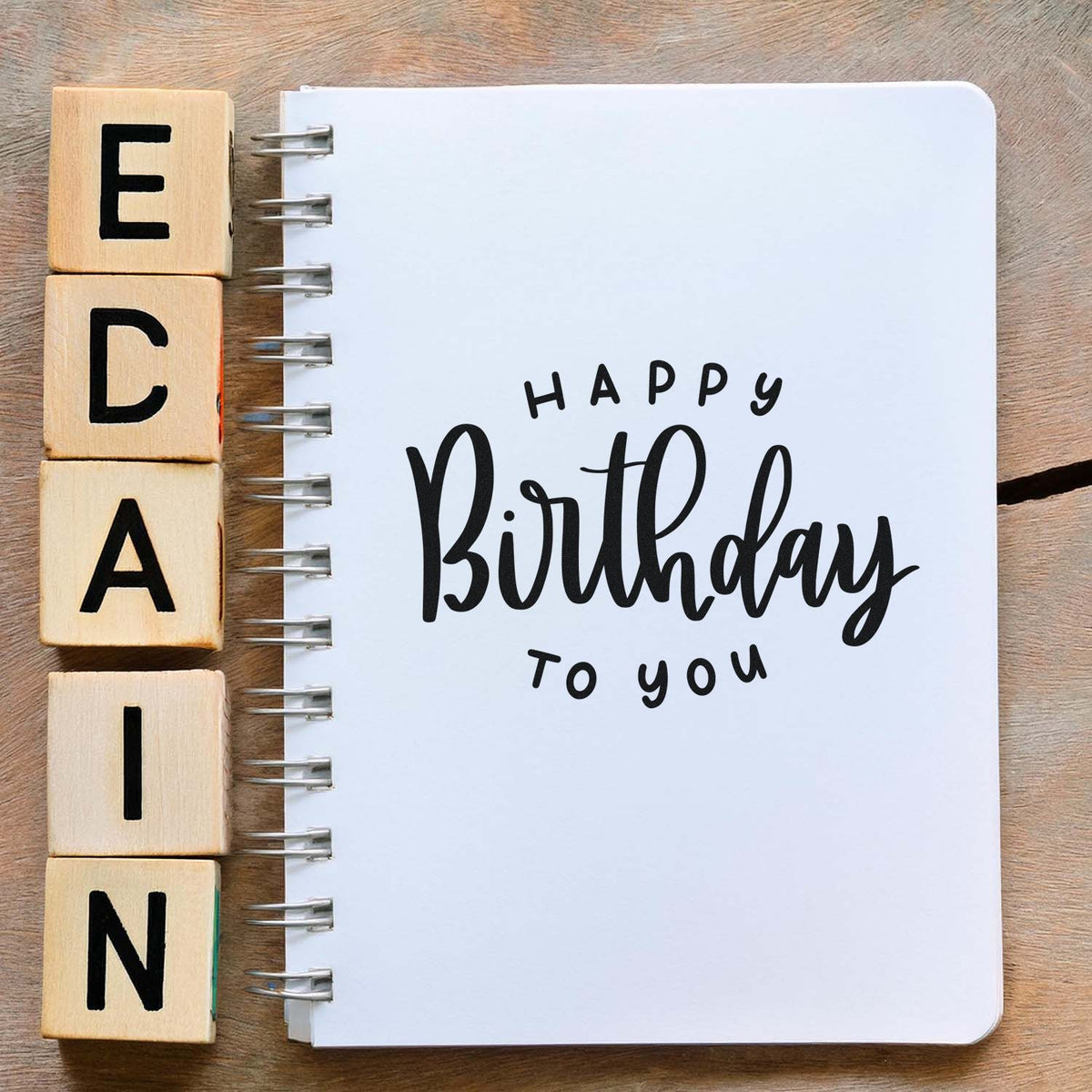 Wooden alphabet stamp blocks beside a white spiral notebook with black Happy Birthday to you stamp lettering.