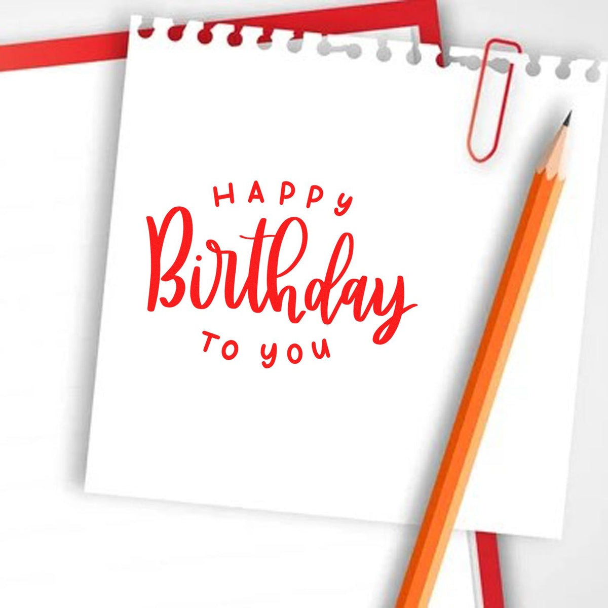 Red Happy Birthday stamp and seal on white notepad, with orange pencil and paperclip.