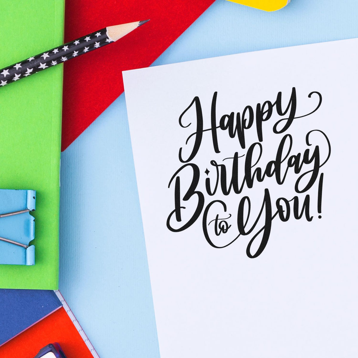 Birthday greeting card with black calligraphy, star-pattern pencil, and colorful stamp-and-seal supplies on bright paper.
