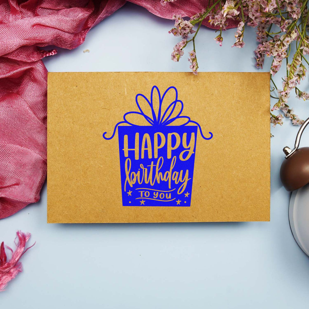 Bright blue happy birthday stamp and seal on tan kraft card, framed by pink flowers and ribbon.