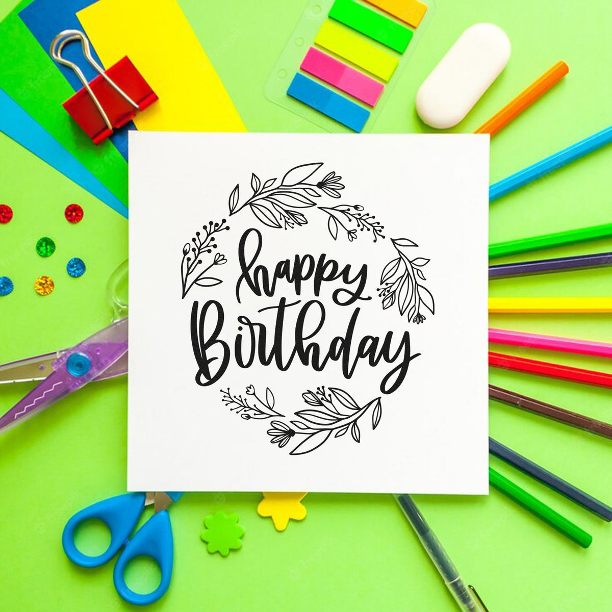 Black floral Happy Birthday stamp and seal design on white card, surrounded by colorful stationery on green background.