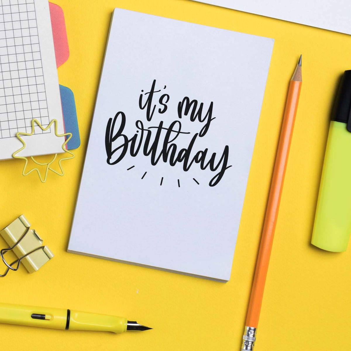 Birthday stamp and seal on white card, with black script, yellow background, orange pencil, neon highlighter, and clips.