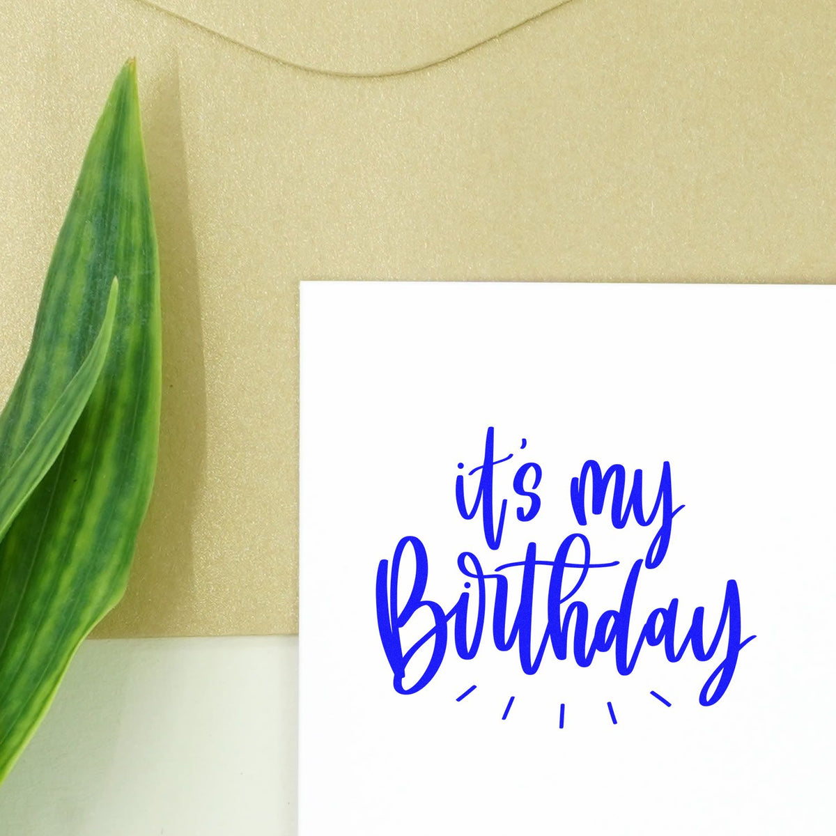Blue Its my Birthday stamp and seal on white card with green leaf, against beige background.