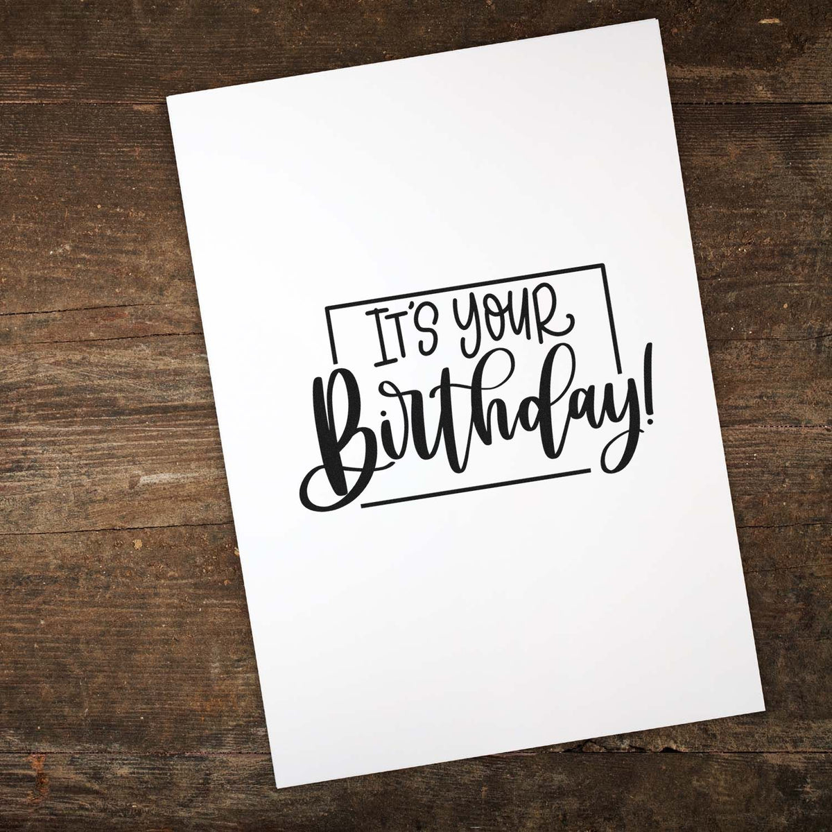 Black birthday stamp and seal on white card over rustic dark wood, reading Its your Birthday!