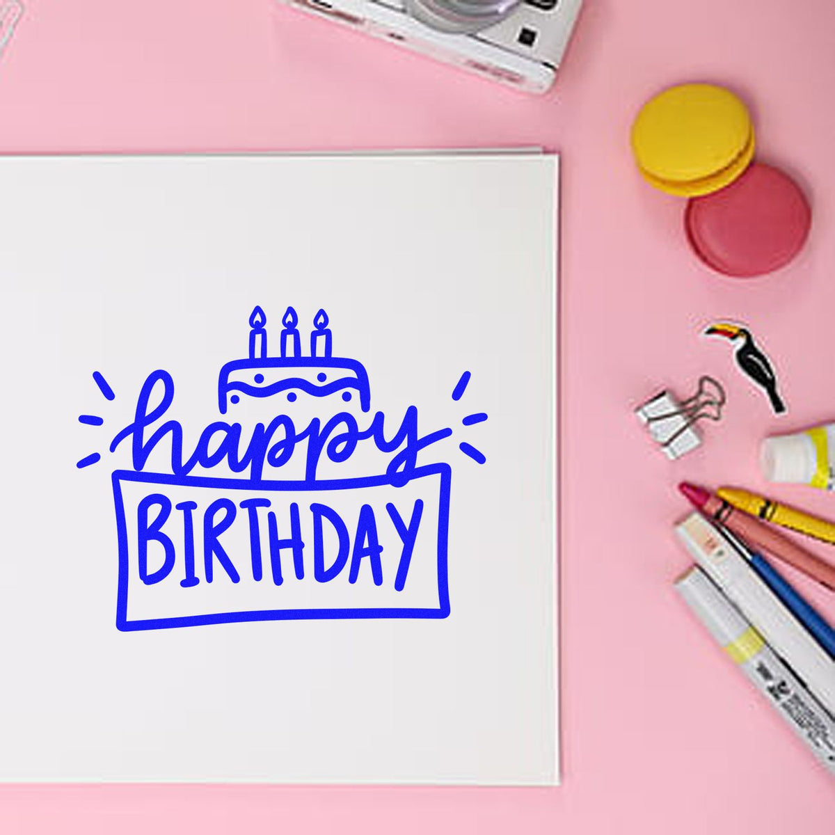 Blue Happy Birthday stamp on white card, surrounded by pink background, colorful seal stamps and markers.