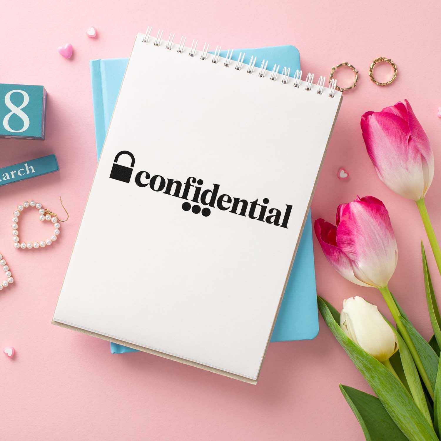 Pink stationery flat lay with a confidential stamp and lock on a white spiral notebook, blue folder, tulips, and gold seals.