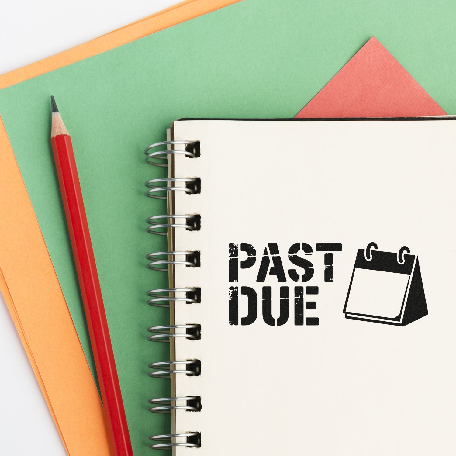 Past due rubber stamp on white spiral notebook, with red pencil and green, orange, coral paper sheets.