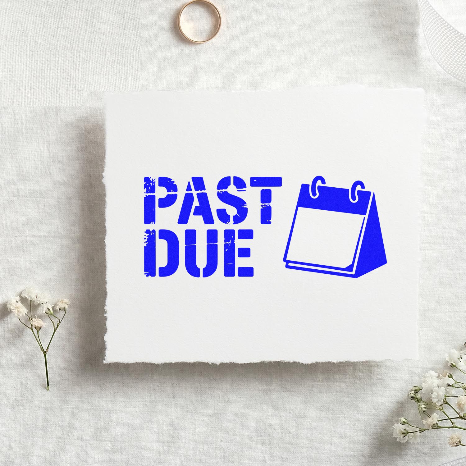 Blue PAST DUE stamp and seal with calendar icon on white paper, on soft white fabric with flowers.