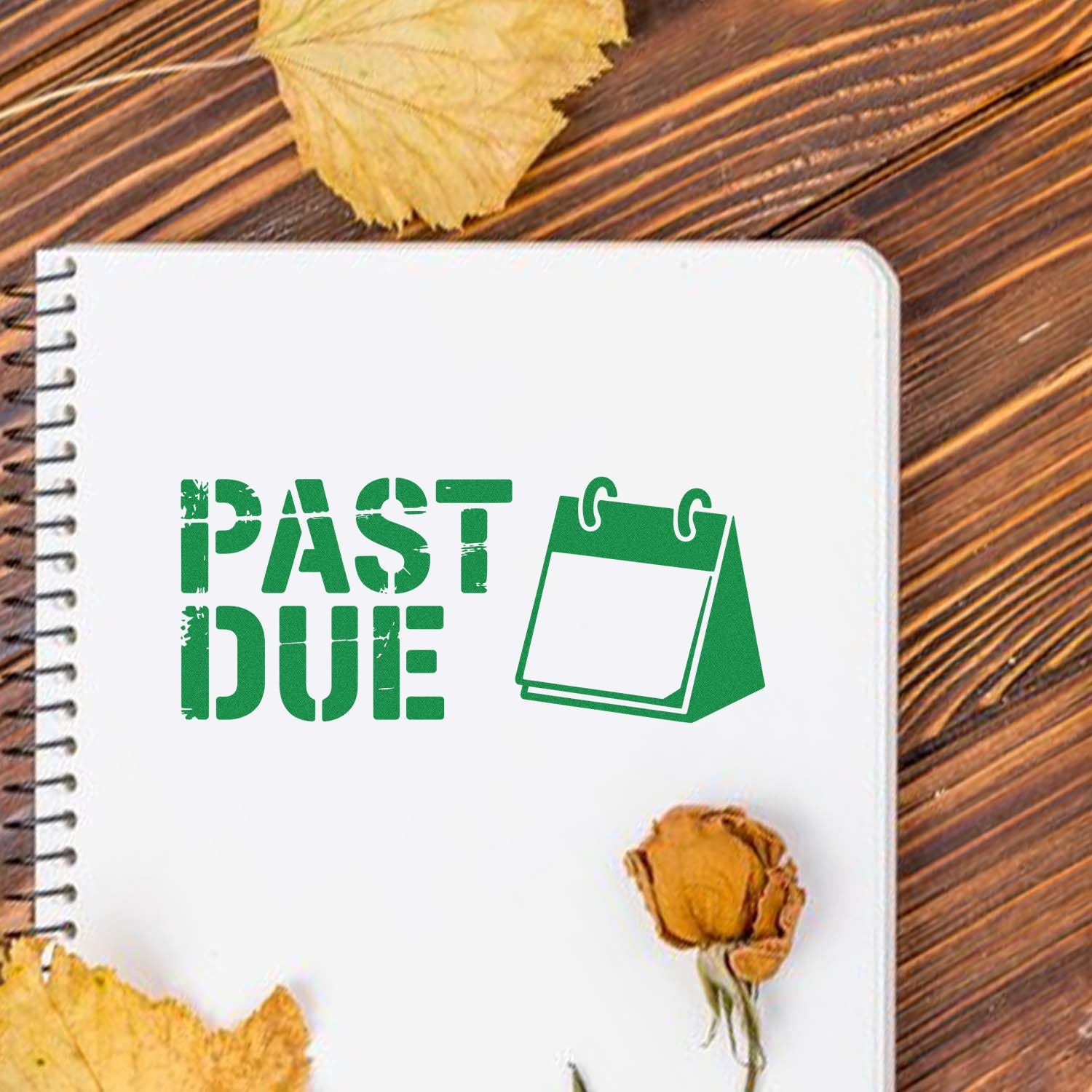 Green PAST DUE stamp and calendar seal on a white spiral notebook, with yellow leaves on a wooden table.