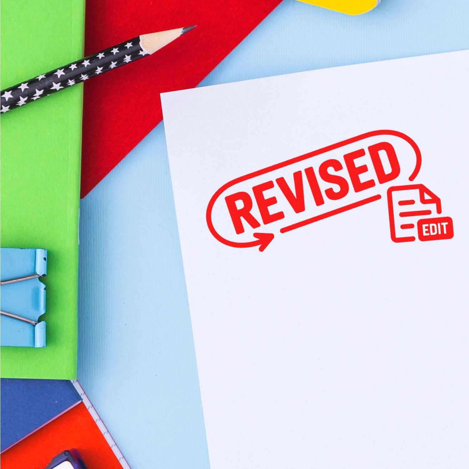 Red REVISED stamp seal on white paper with edit icon, surrounded by colorful stationery and a star-pattern pencil.