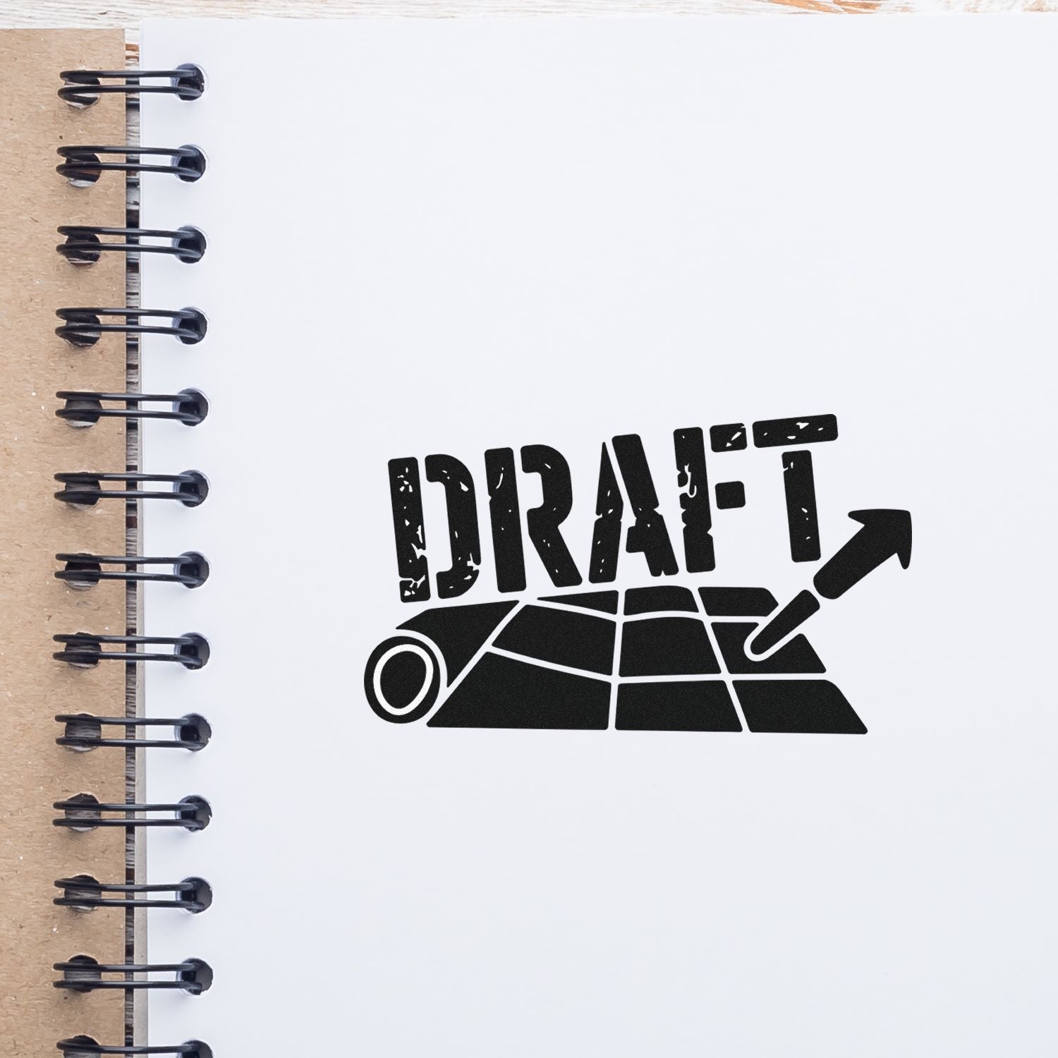 Black DRAFT stamp seal over rolled blueprint icon on white notebook page with spiral binding and brown cardboard edge