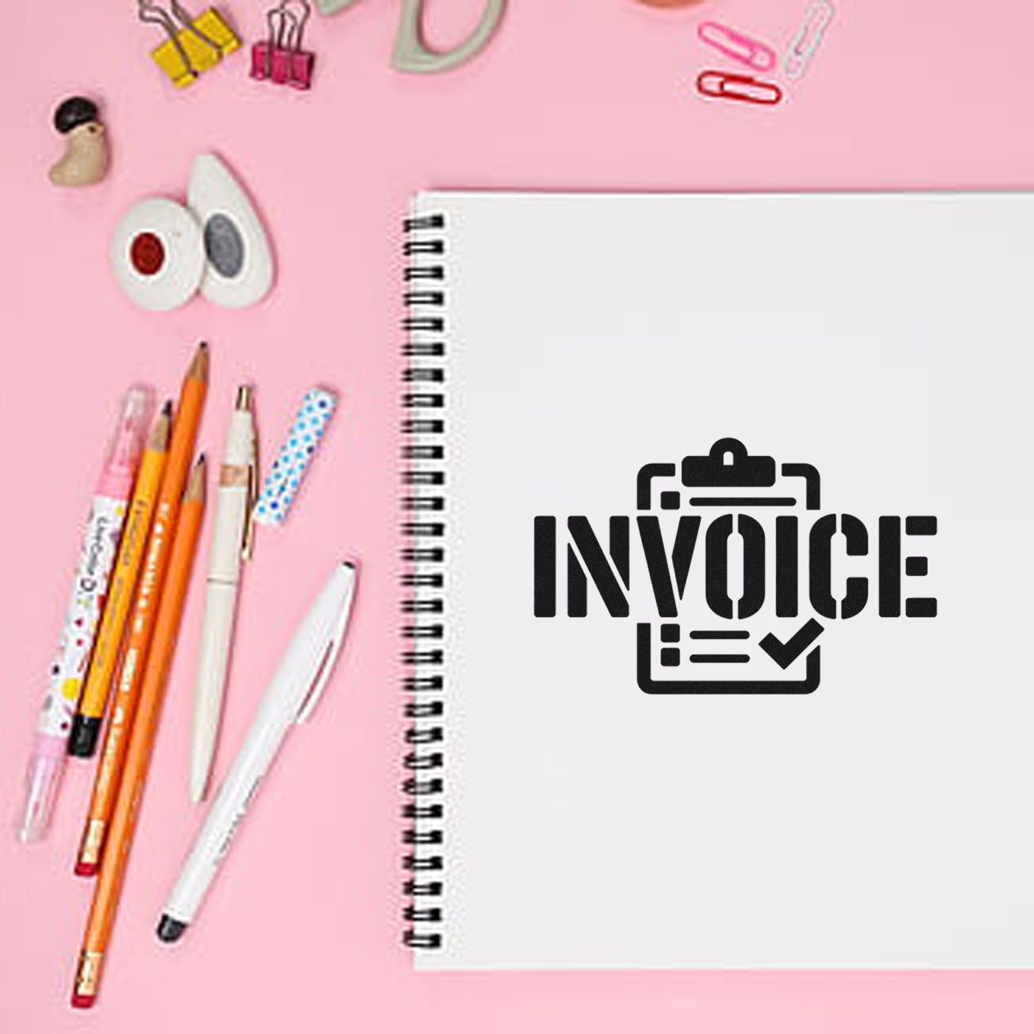 Pink desk flat lay with spiral notebook stamped INVOICE in black, plus pens, binder clips, and seal products.