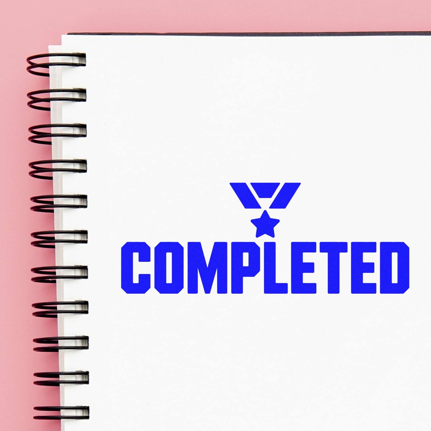 Blue COMPLETED stamp with star seal on white spiral notebook, set against a pink background.