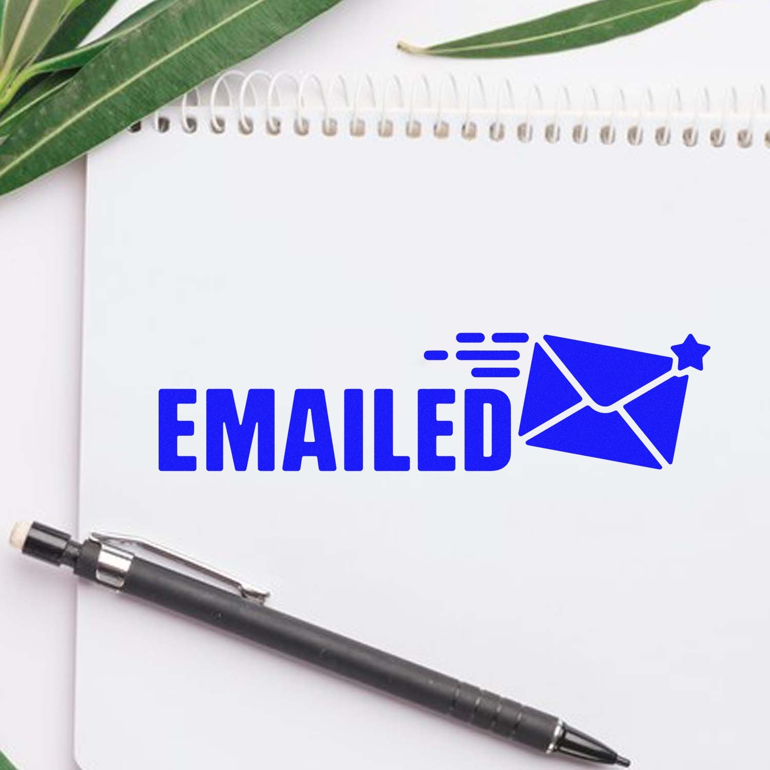 Blue EMAILED stamp seal with envelope icon on a white notebook, beside a black pen and green leaves