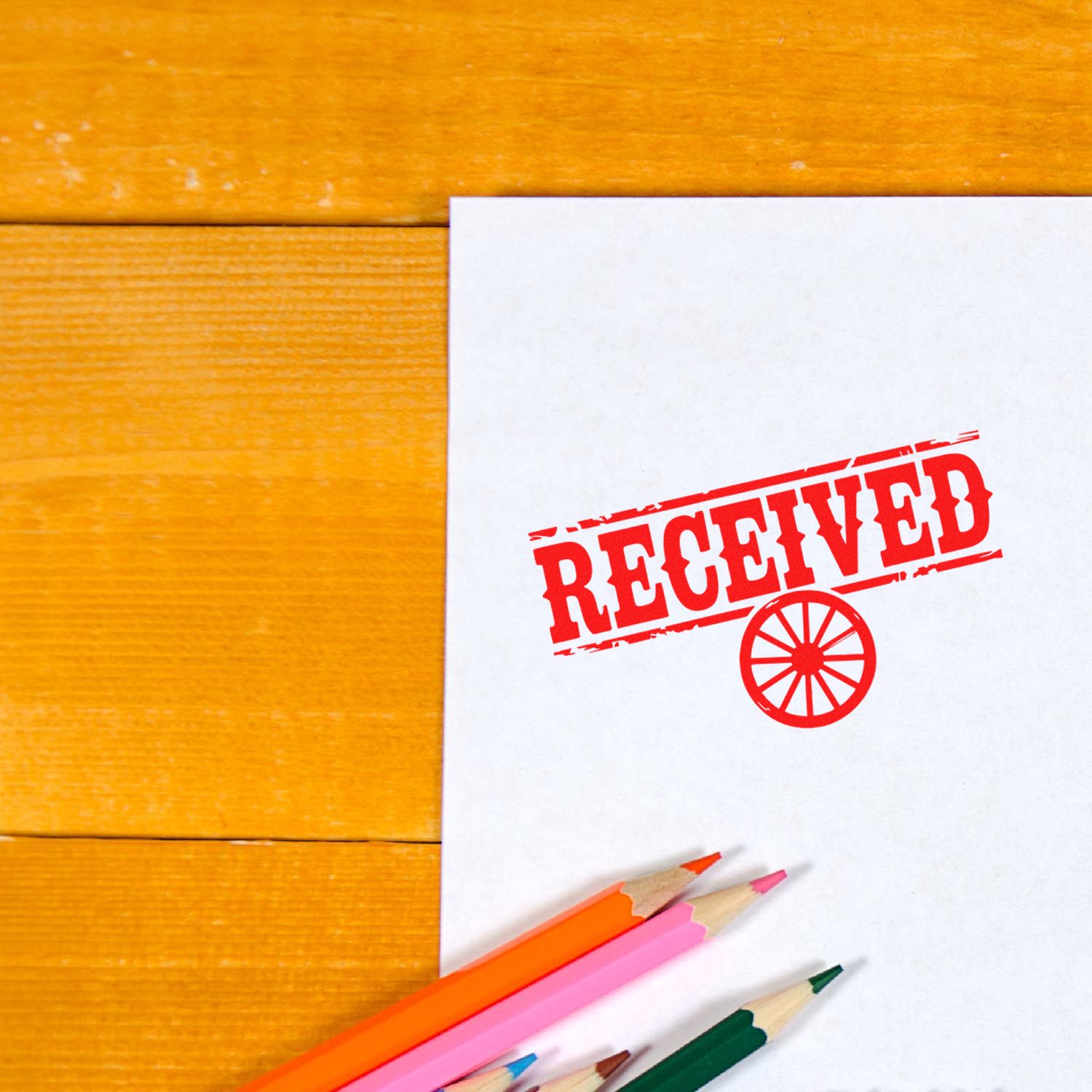 White paper with red RECEIVED stamp and seal icon on wood desk, with colored pencils.
