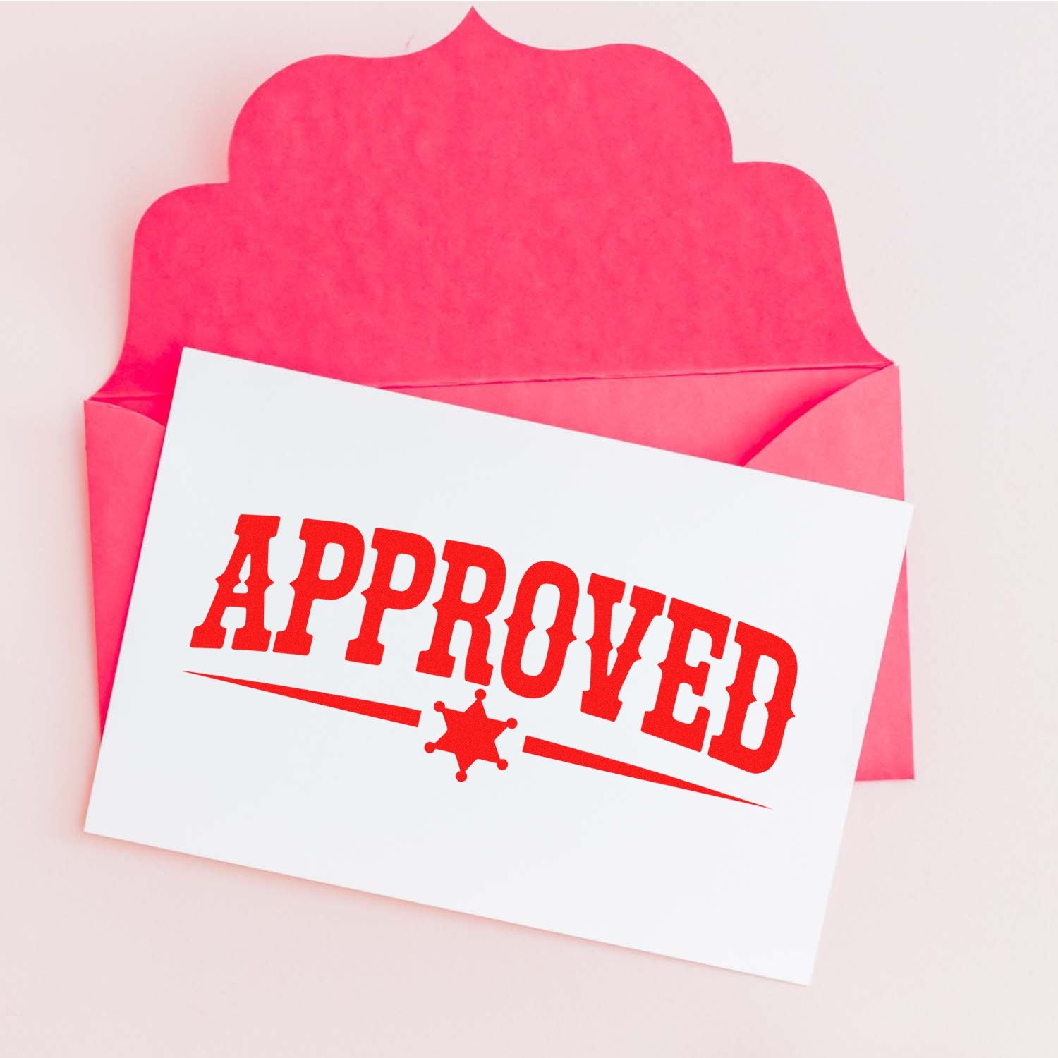 Pink envelope with white card and red APPROVED stamp seal, showing a bold approval mark