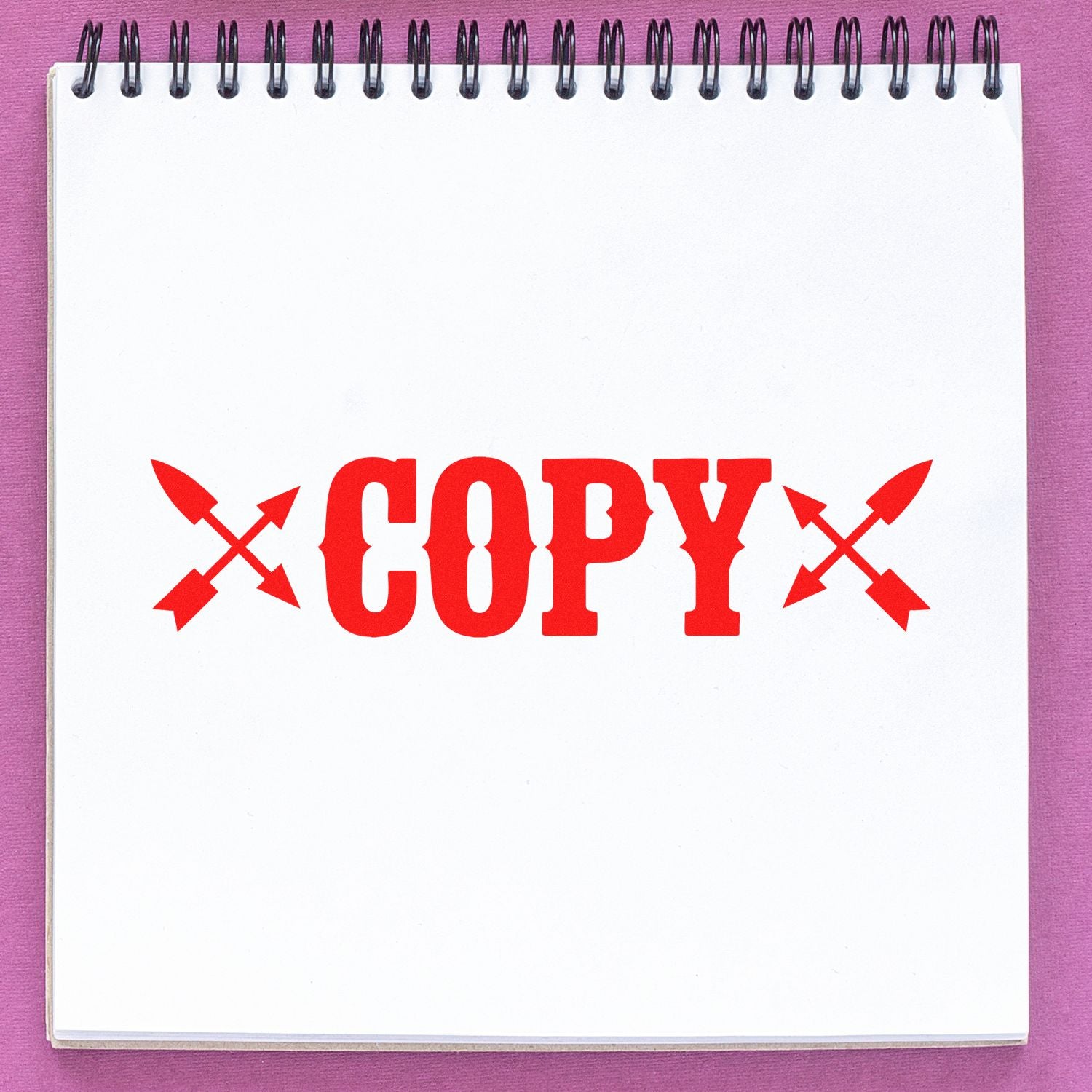 Red COPY stamp seal with crossed arrows on a white spiral notebook, on a pink background.