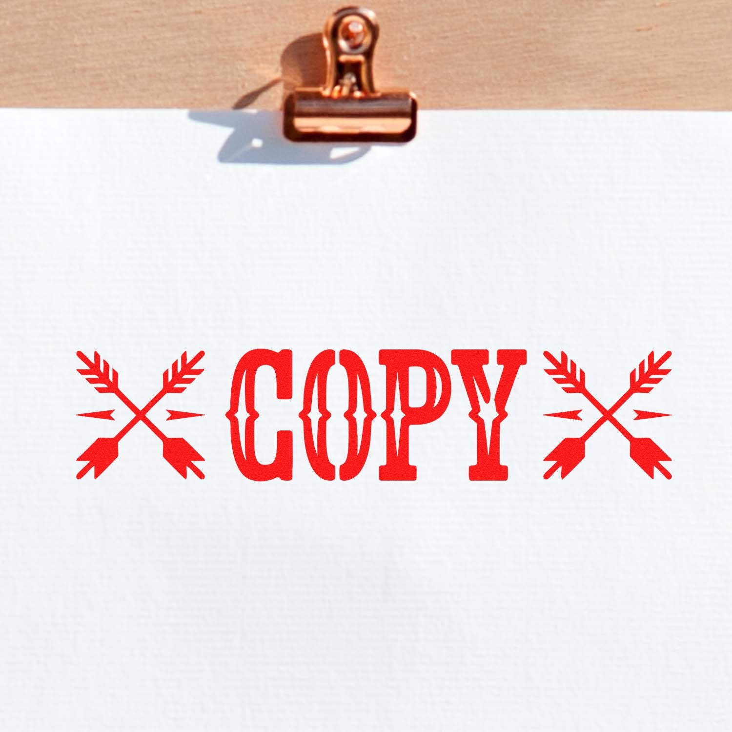 Copper clipboard clip holding white paper with red COPY stamp and crossed-arrow seal design.
