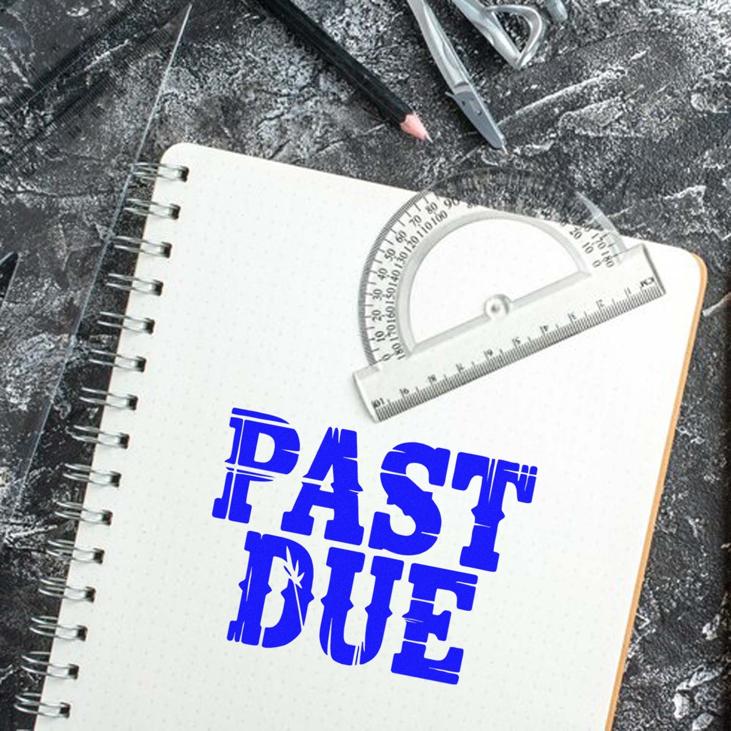 Blue PAST DUE stamp on white spiral notebook with drafting compass, ruler, and clear seal tools on dark stone.