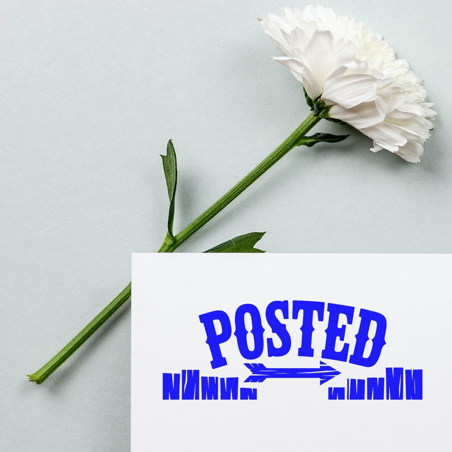 White flower on pale gray background beside a white card with a blue POSTED stamp and seal.