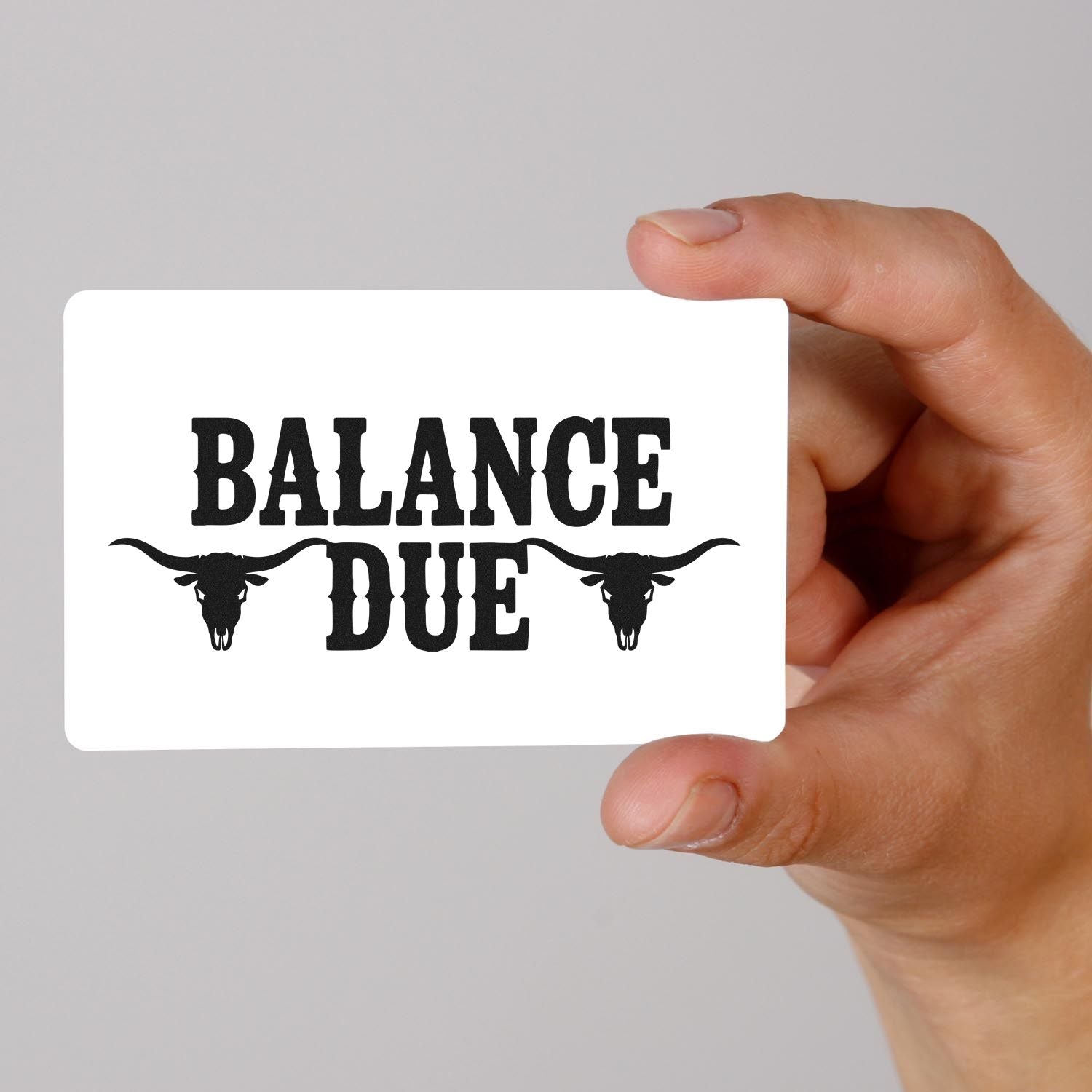 Hand holding white custom stamp card with black BALANCE DUE text and longhorn skull graphics.