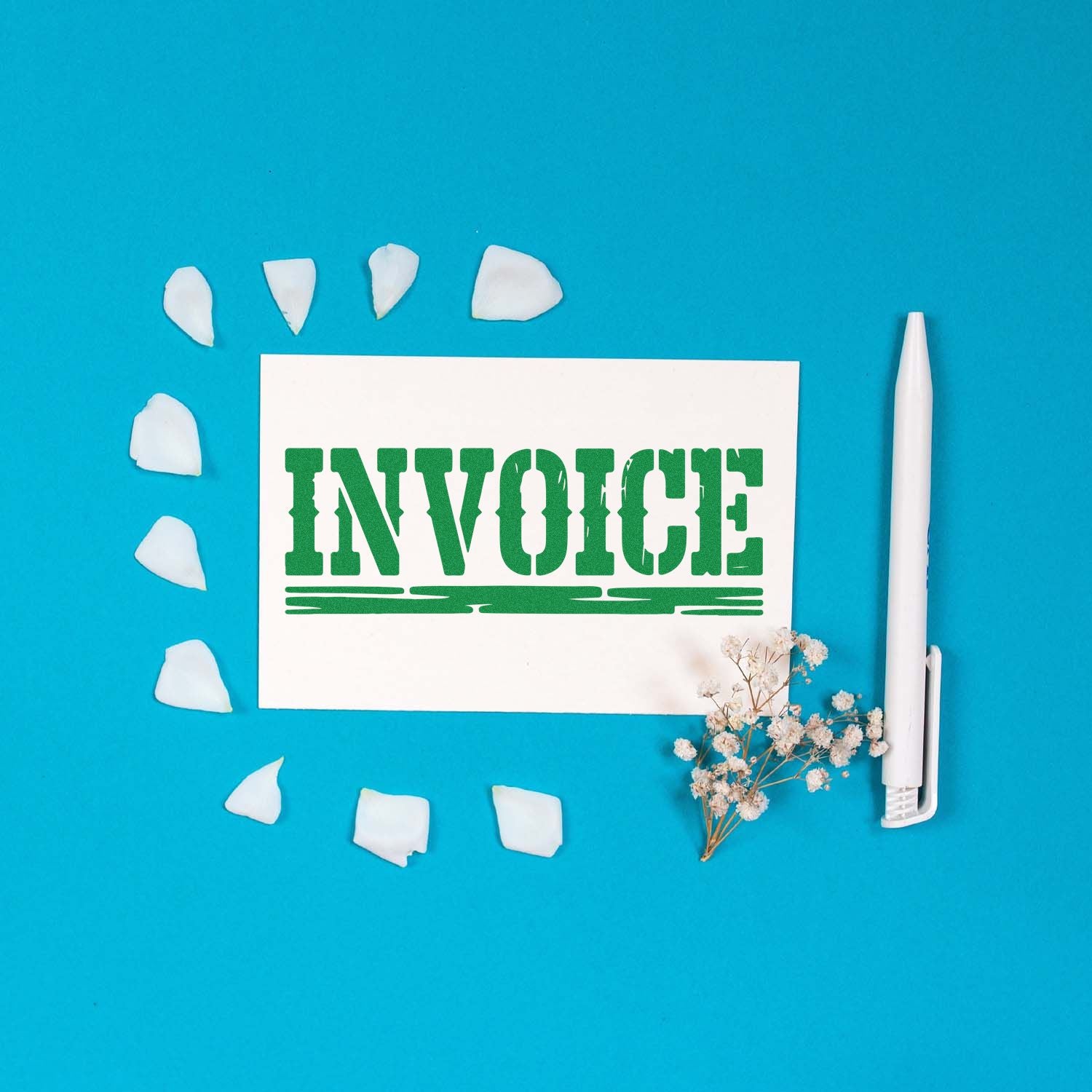 Green INVOICE stamp on white card with white pen, blue background, scattered white seal pieces and dried flowers.