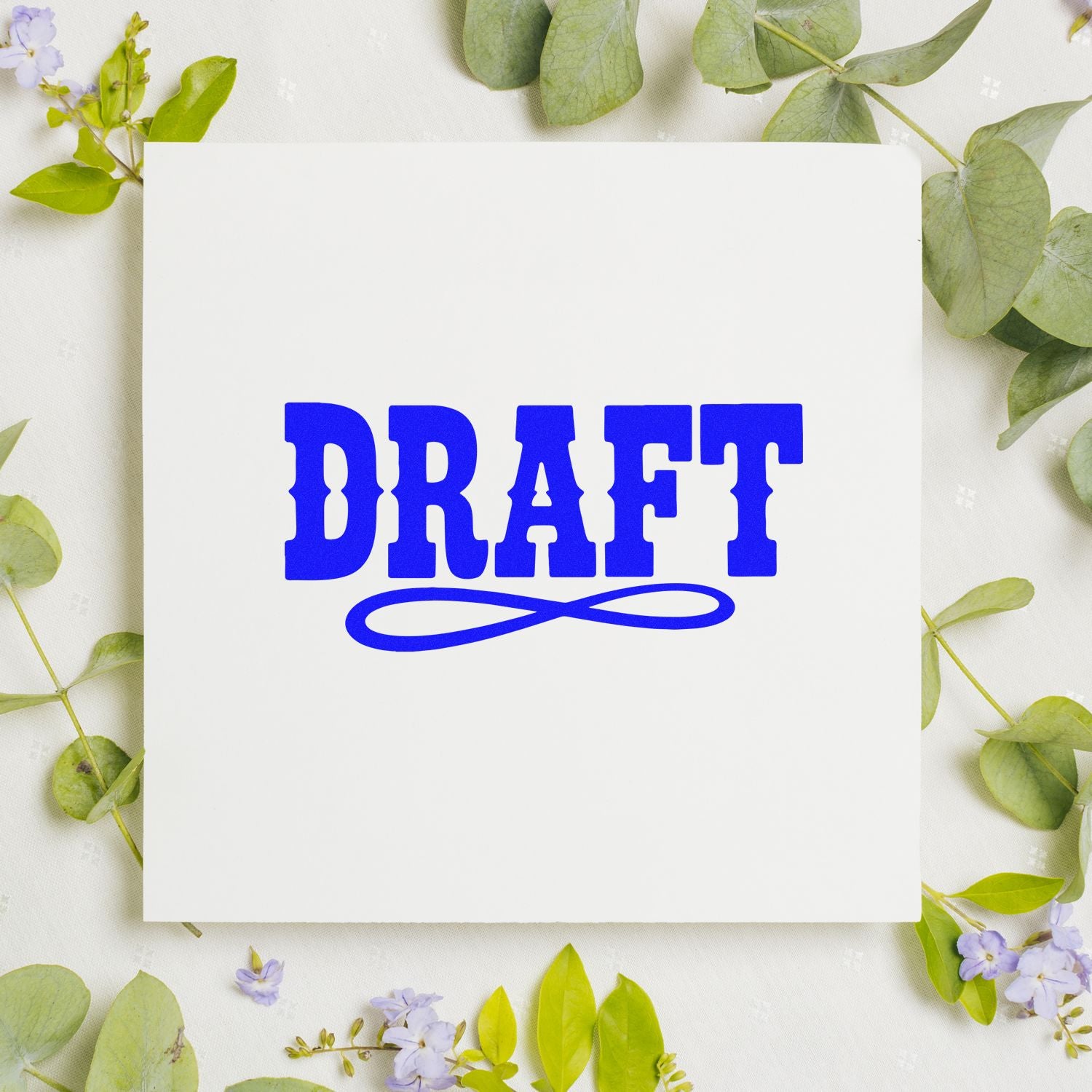 Blue DRAFT rubber stamp seal on white card, surrounded by green leaves and small lavender flowers.
