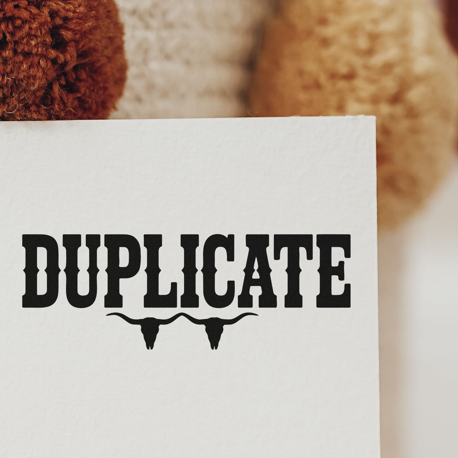 Black DUPLICATE stamp and bull skull seal on white paper, with warm brown textured background.