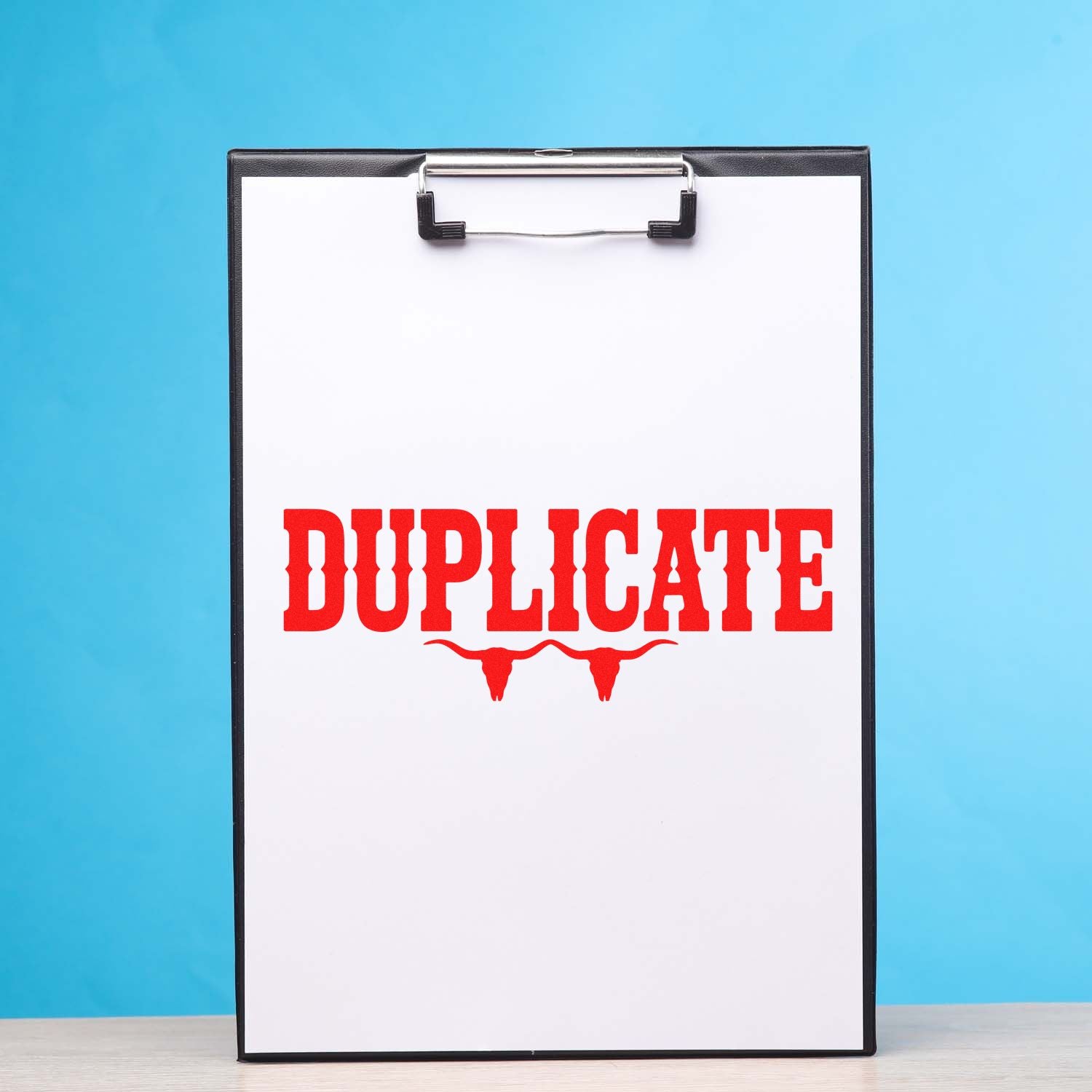 Clipboard with bold red DUPLICATE stamp and bull skull seal on white paper, set against a blue background.