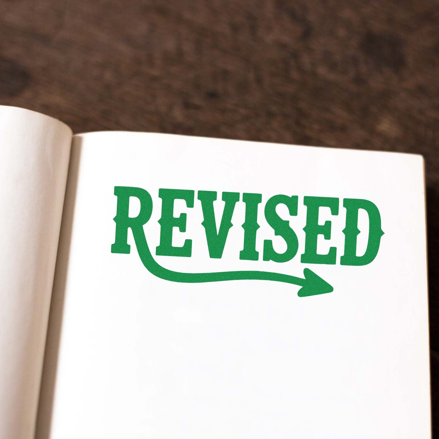Green REVISED stamp with arrow seal on a white page, featuring bold green lettering and a curved underline arrow.
