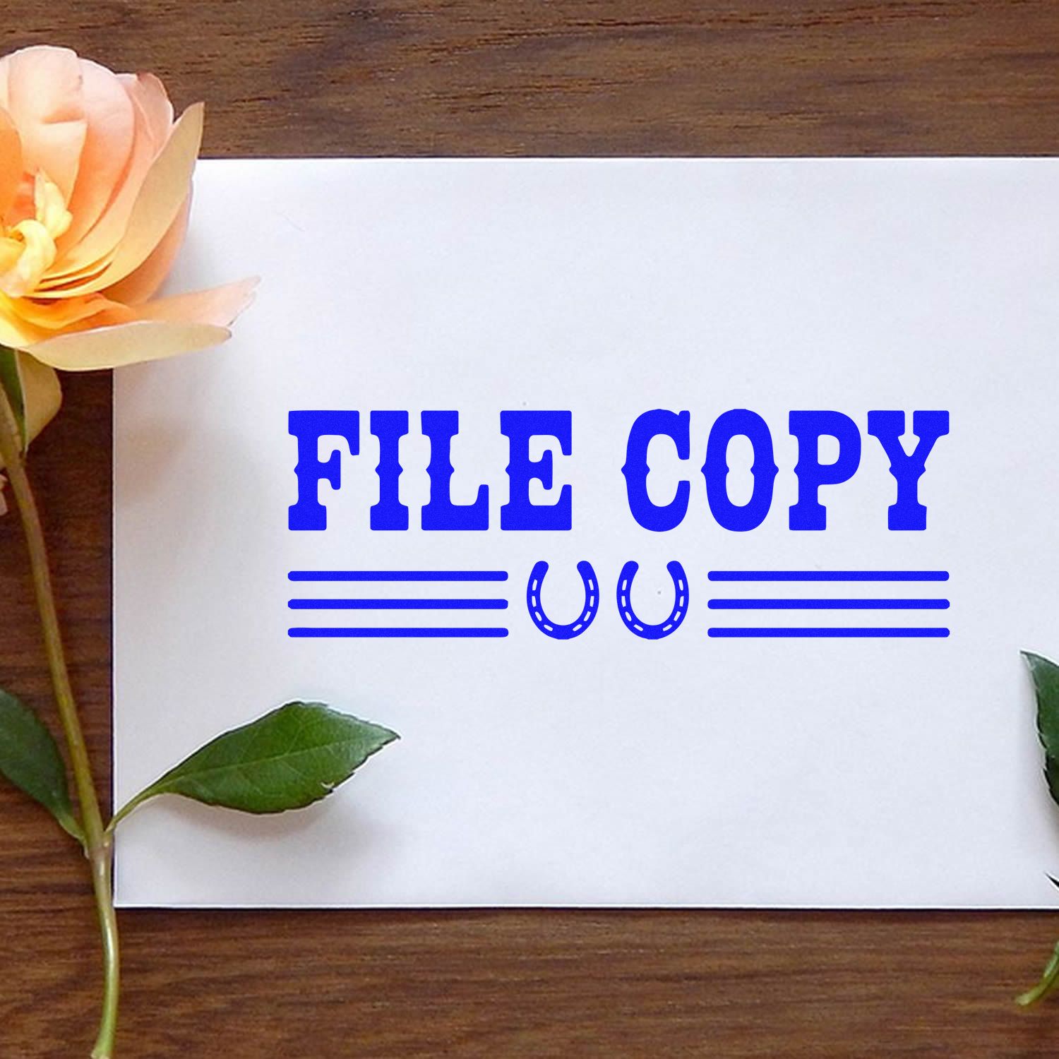 Blue FILE COPY rubber stamp with horseshoe seal icons on white paper, beside a peach flower on a wood table.