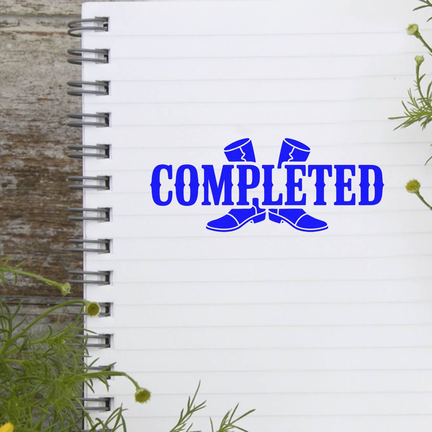Blue COMPLETED stamp and seal on a white spiral notebook page, with rustic wood background and green foliage.
