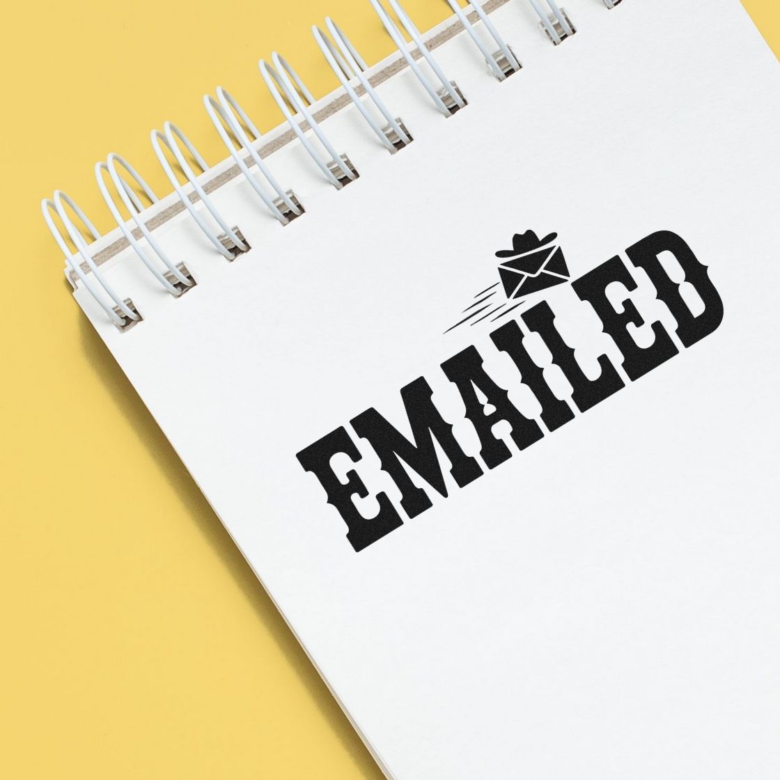 White spiral notebook with black EMAILED rubber stamp and envelope seal on yellow background