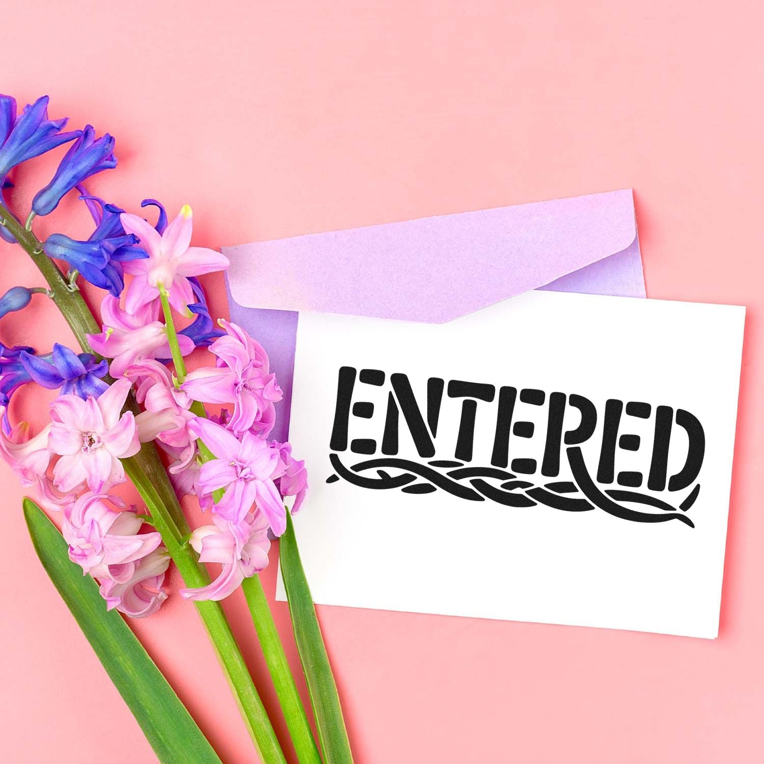 Black ENTERED rubber stamp on white card, with lavender envelope and pink-purple flowers on a pastel pink background.