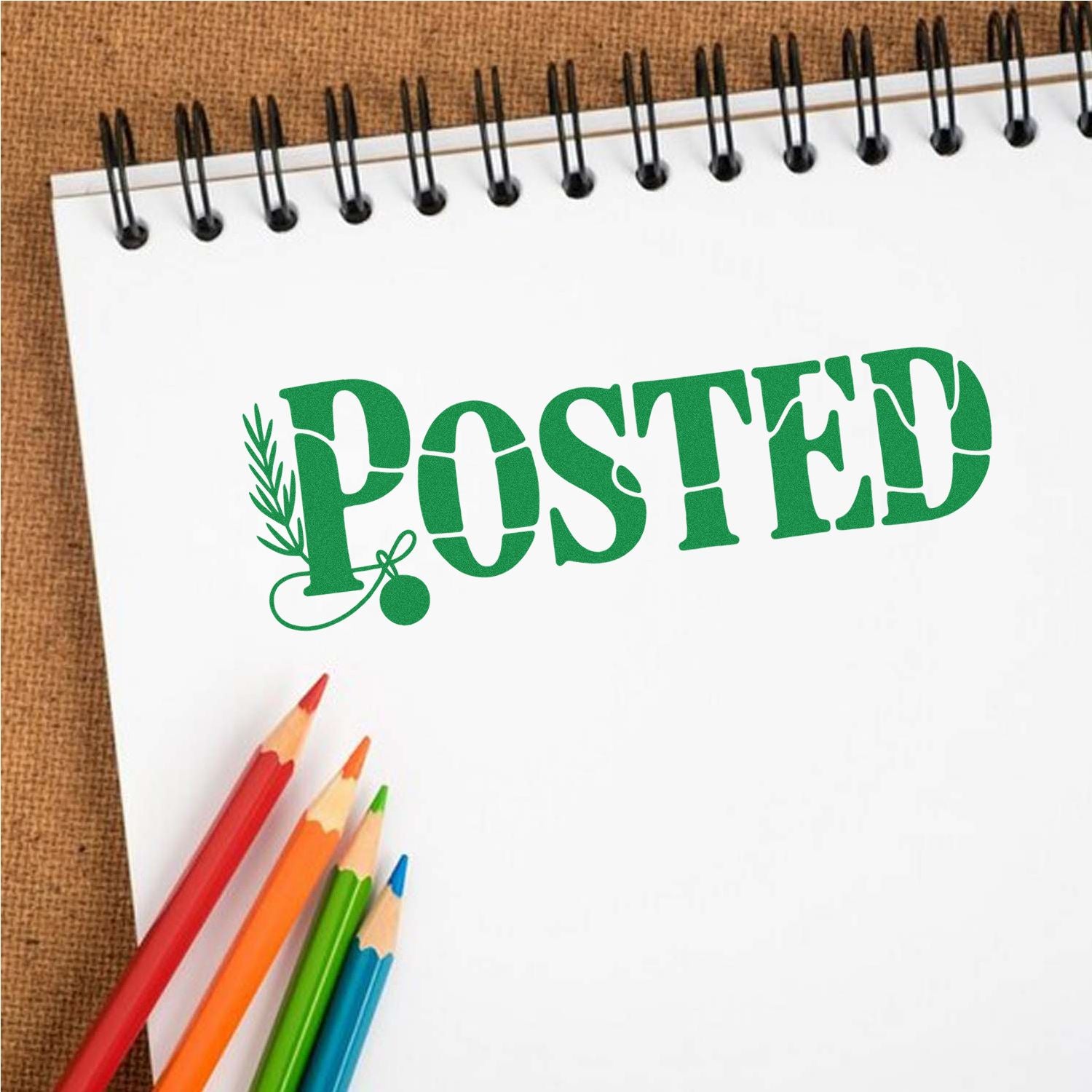 Green POSTED stamp on white spiral notebook with colorful pencils against a brown textured background