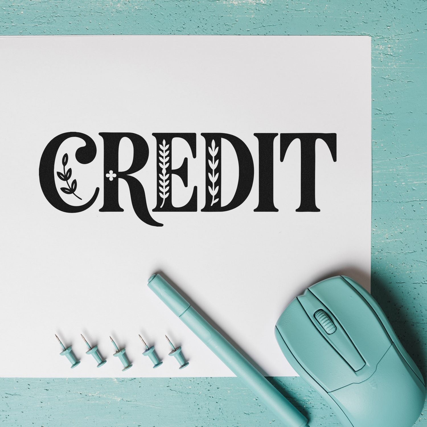 Black decorative CREDIT lettering on white paper with mint stamp seal, embossing pen, and aqua tools on turquoise background.