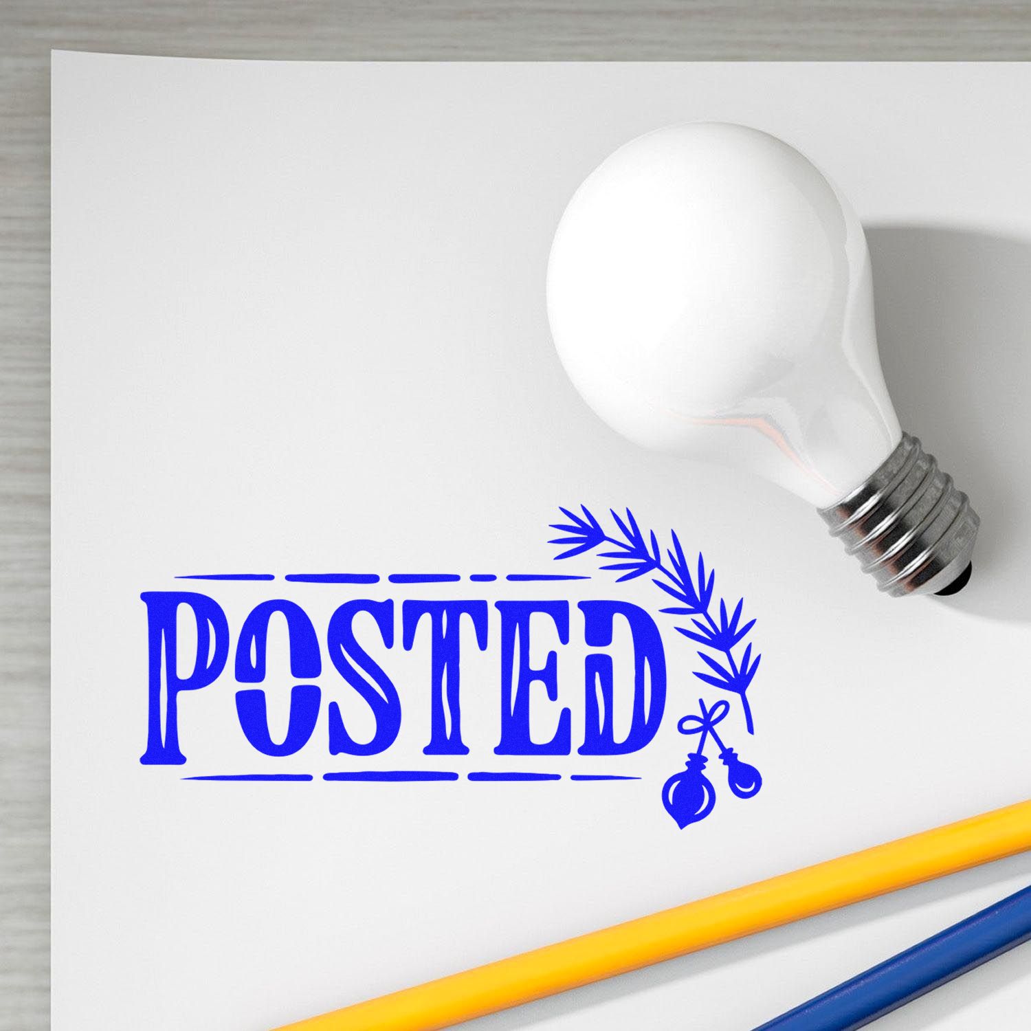 White lightbulb-shaped stamp seal product with blue POSTED text, leaf accent, and yellow-blue pencils on white paper.