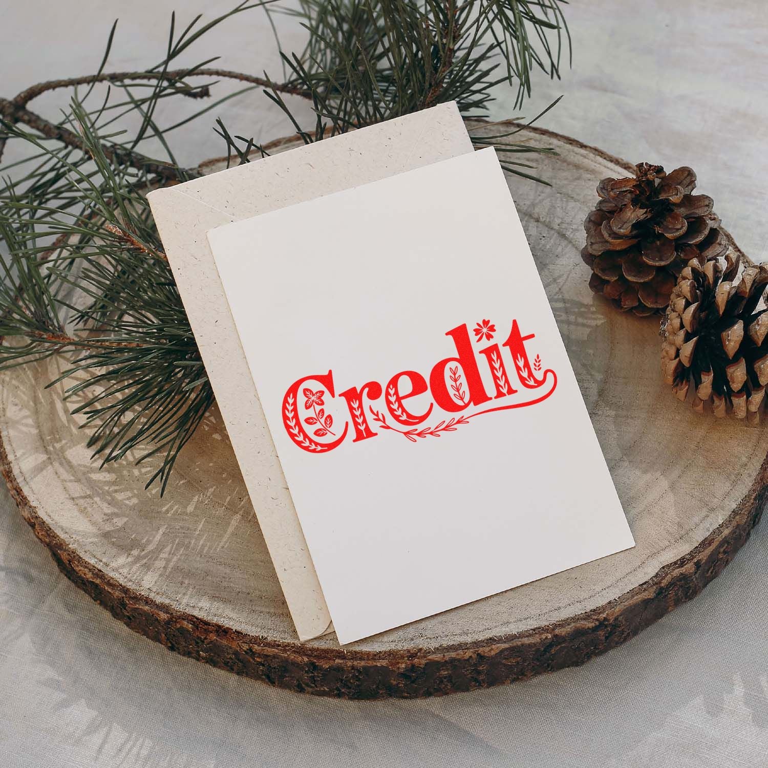 White stamp and seal card with red Credit lettering, pine branches, pinecones, and a rustic wood slice background.