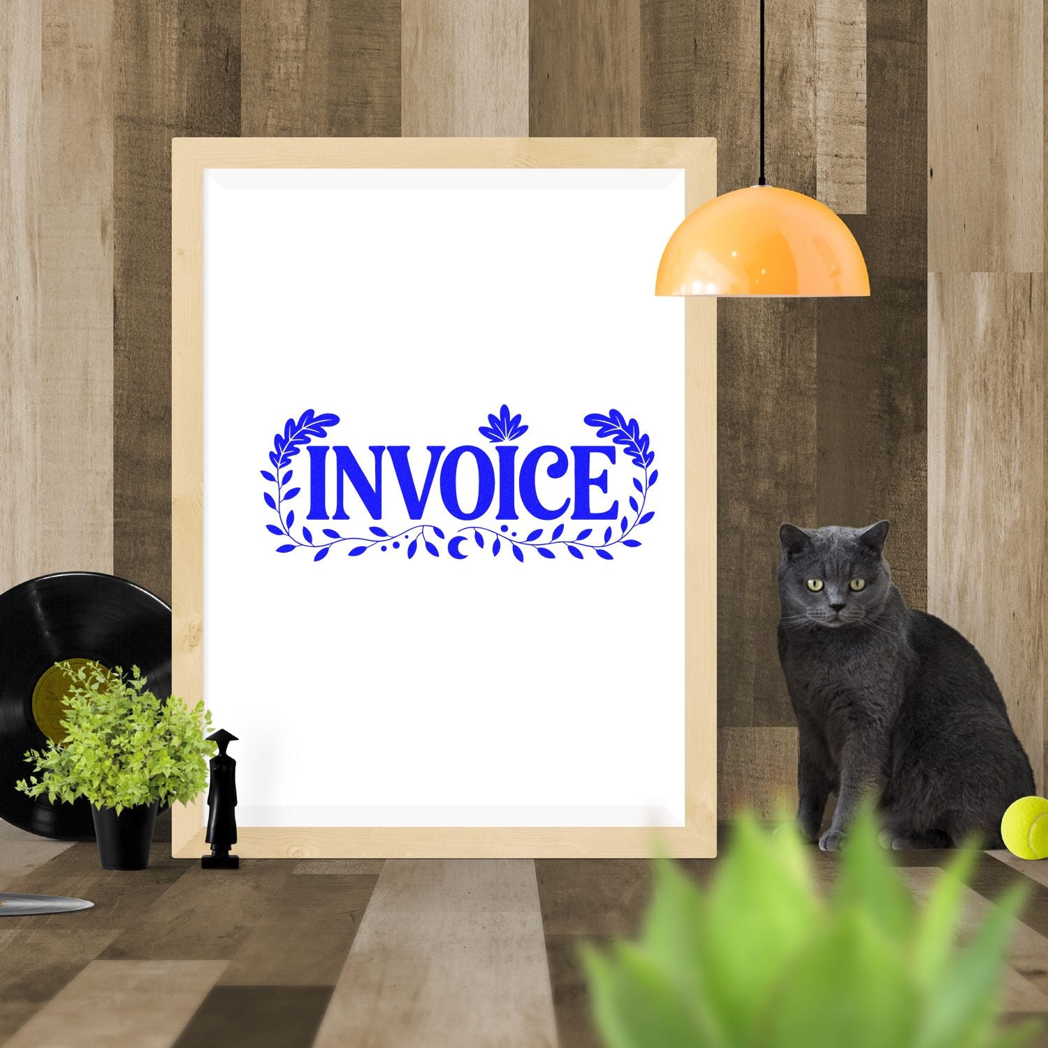 Blue invoice stamp seal with leaf border on a white framed poster, styled with wood wall, orange lamp, and gray cat.