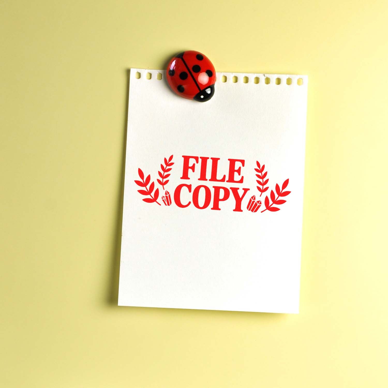 Red FILE COPY rubber stamp seal on white notepad, topped with a ladybug clip, against a pale yellow background.