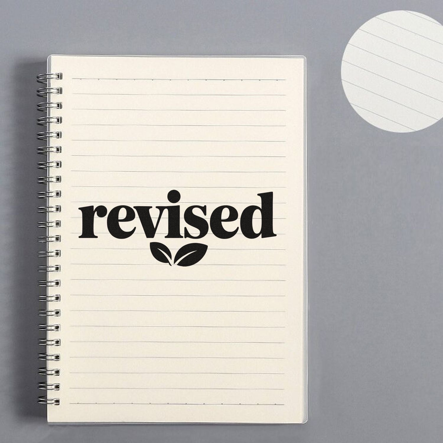 Black revised stamp with leaf icon on cream spiral notebook; gray background, with round lined seal sample.