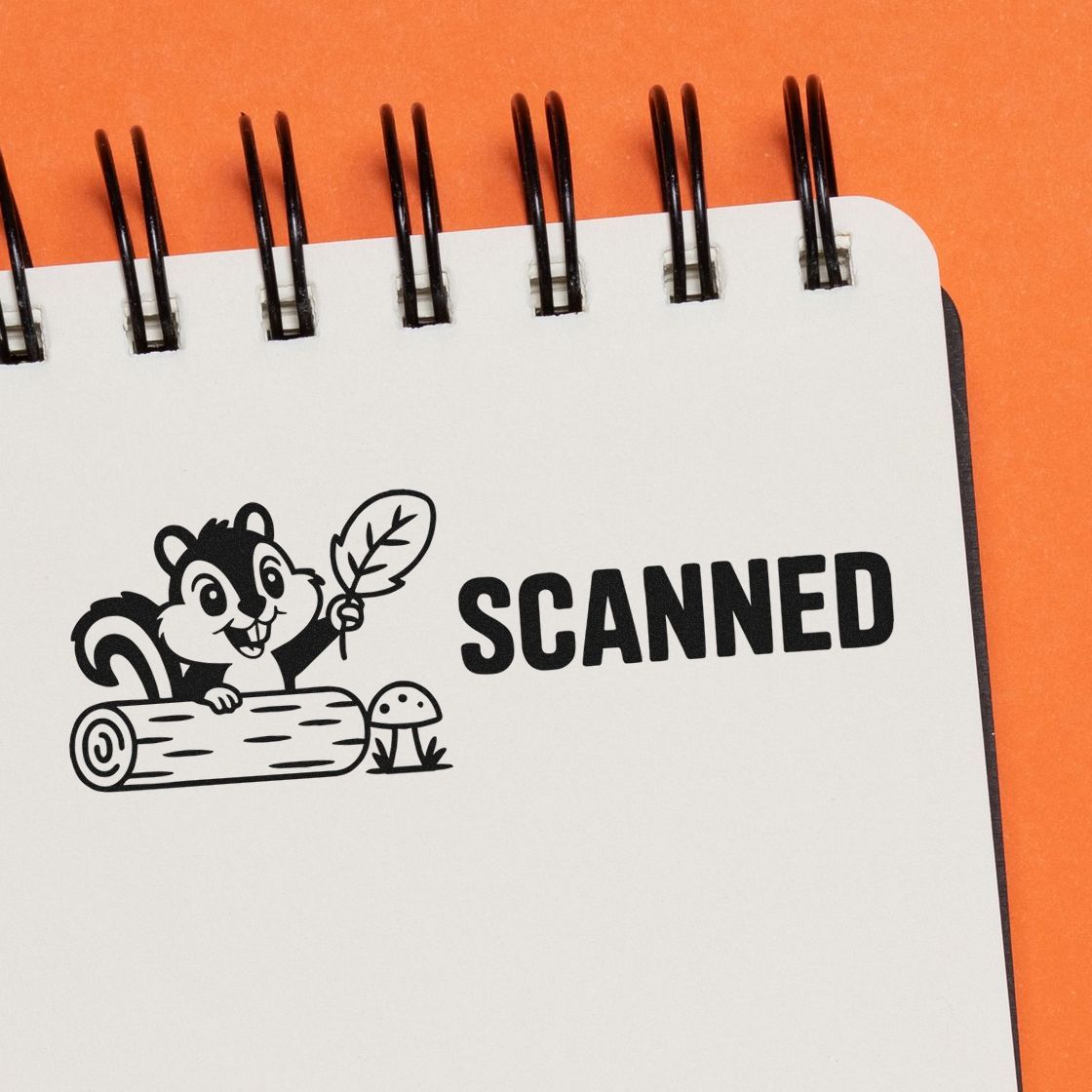 Black SCANNED stamp and seal with squirrel holding a leaf on a white spiral notebook, on a bright orange background.