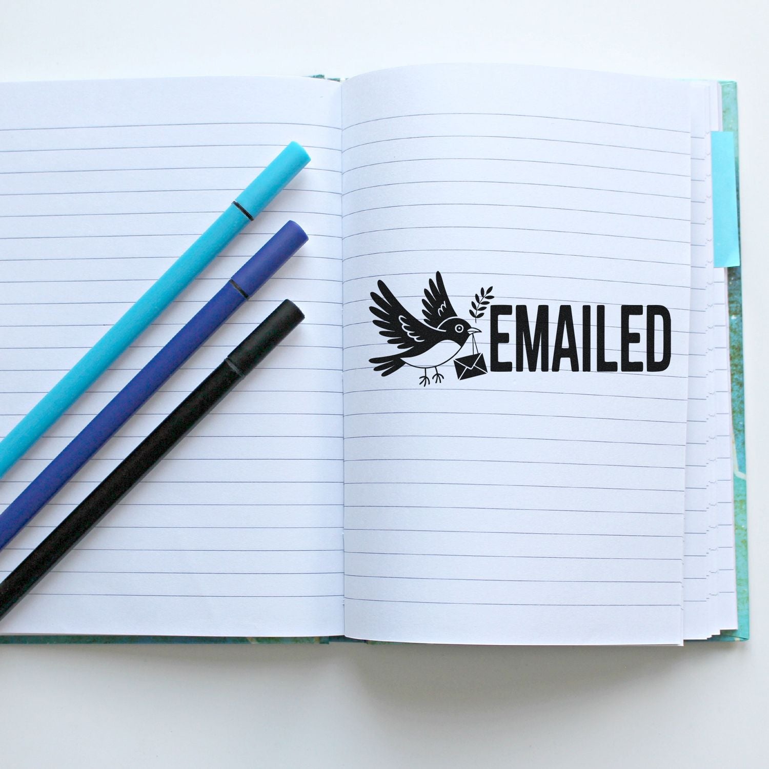 Open lined notebook with black bird EMAILED stamp seal and turquoise, purple, and black pens.