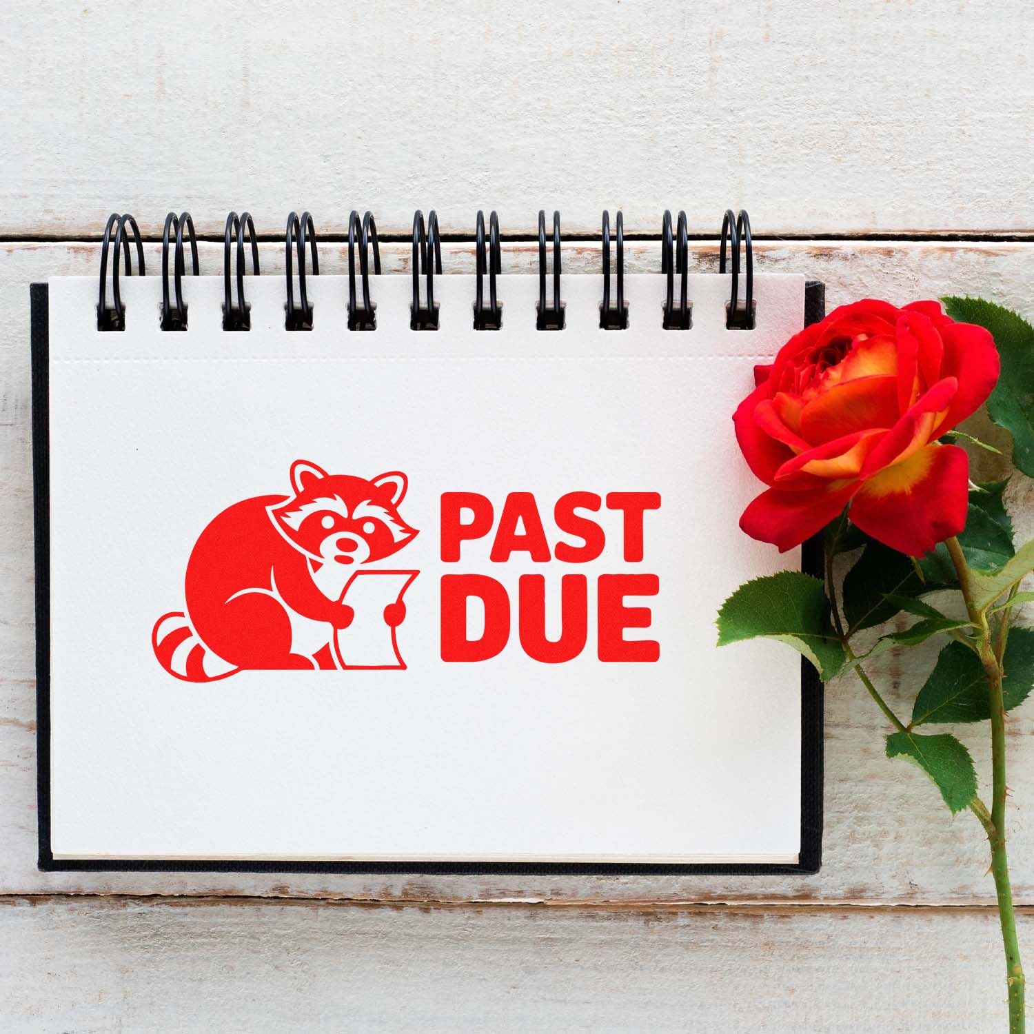 Red PAST DUE stamp and seal with raccoon on white spiral notebook beside a red rose.