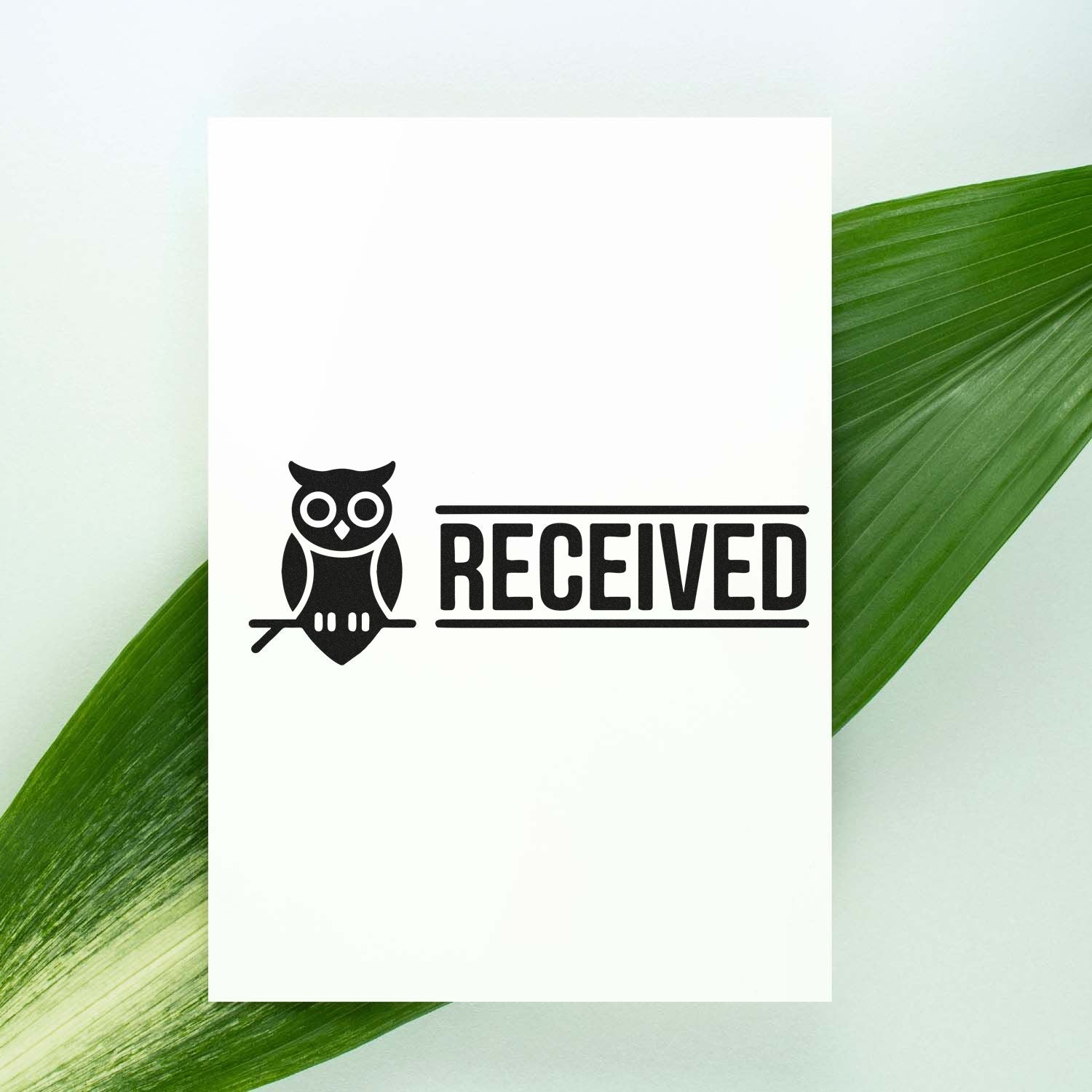 Black RECEIVED stamp and owl seal on a white card, set against green leaves.